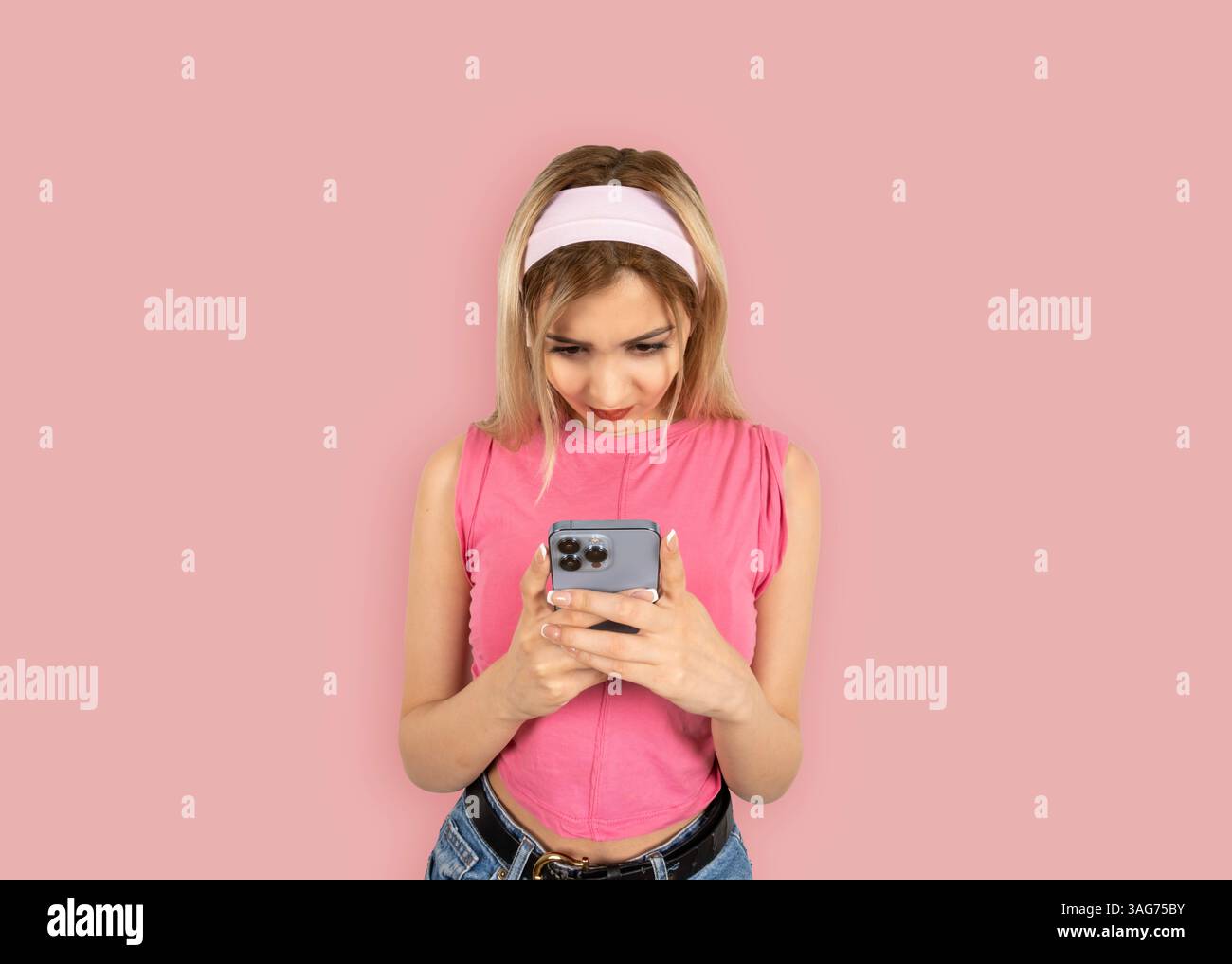 ritratto di una donna bionda sicura di sé che usa lo smartphone. Indossa una camicia rosa senza maniche che regge il telefono cellulare, digita, invia messaggi, naviga Foto Stock