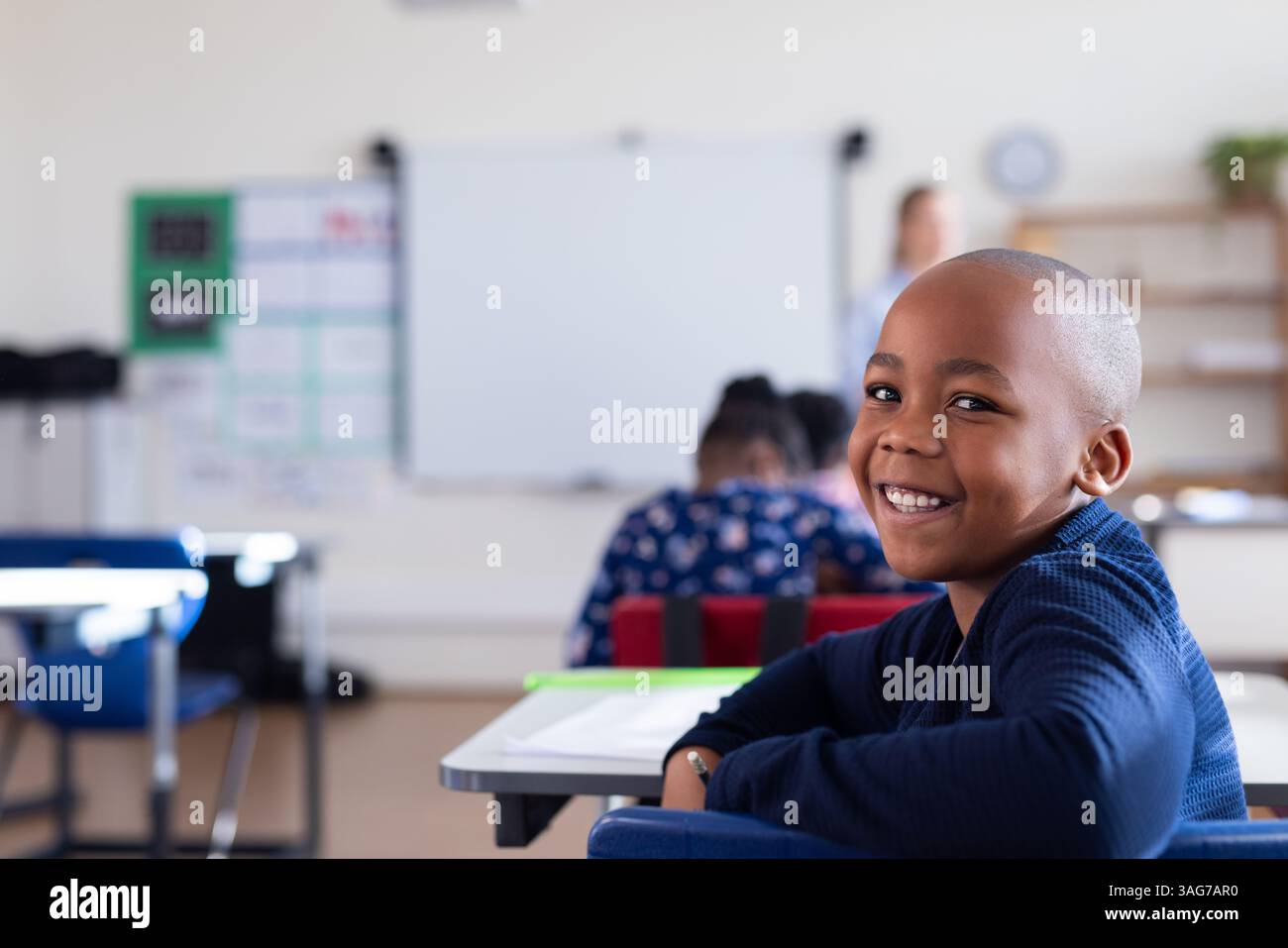 Sorridente ragazzo afroamericano seduto alla scrivania in classe, godendo dell'ambiente scolastico Foto Stock