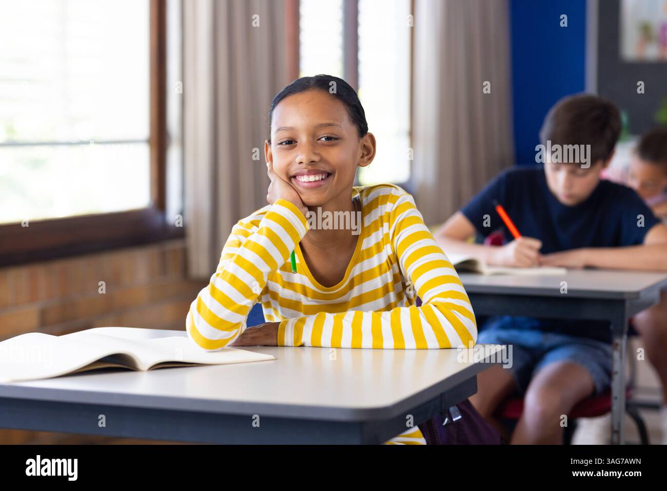 Ragazza sorridente seduta alla scrivania con libro aperto in classe Foto Stock