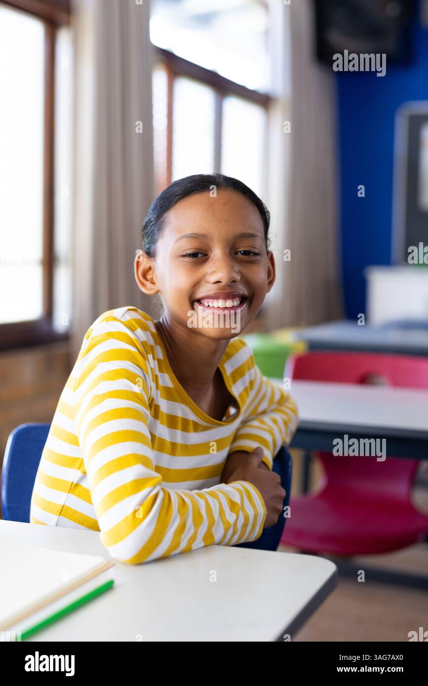 Ragazza sorridente seduta alla scrivania in classe a guardare la macchina fotografica Foto Stock