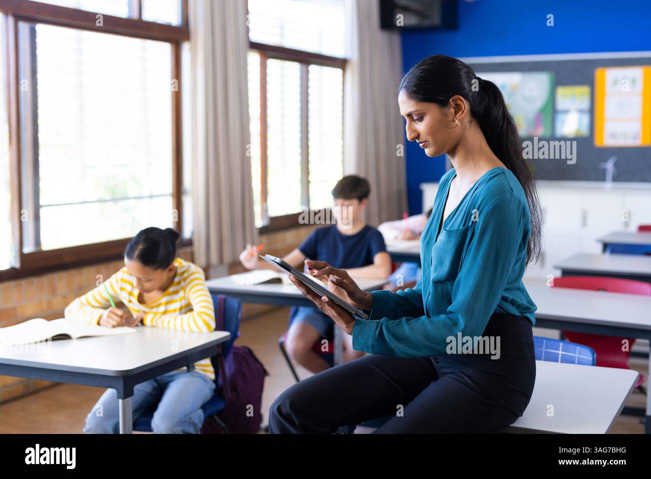 A scuola, insegnante indiana femminile che usa il tablet mentre gli studenti studiano in classe, copia spazio Foto Stock