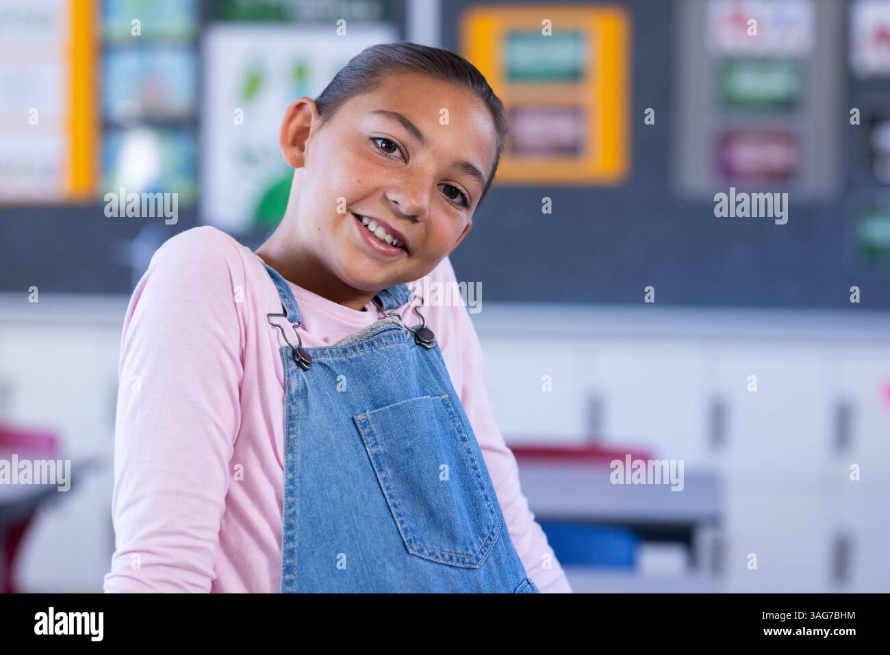 Ragazza sorridente in tuta che posa con sicurezza in classe a scuola Foto Stock