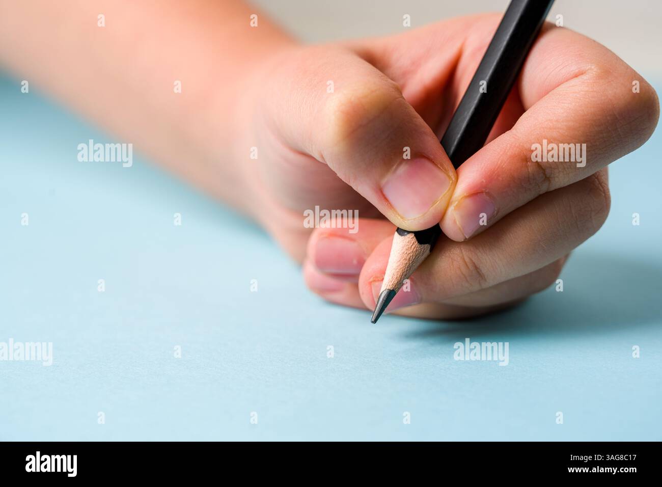 Mano sinistra con una penna a sfera su un blocco appunti aperto su sfondo blu Foto Stock