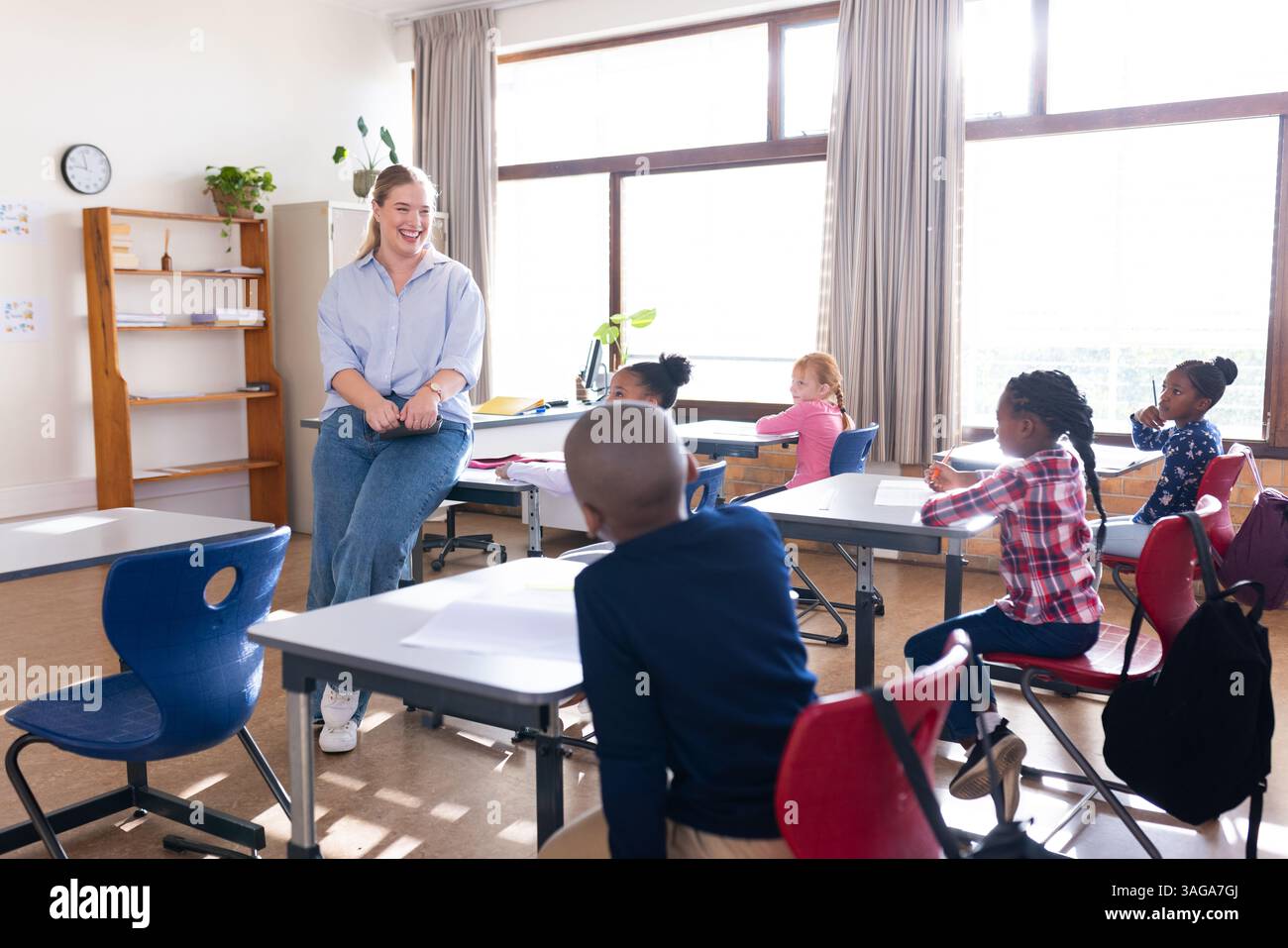 Insegnante femminile che promuove un ambiente di apprendimento interattivo con studenti diversi in classe scolastica Foto Stock