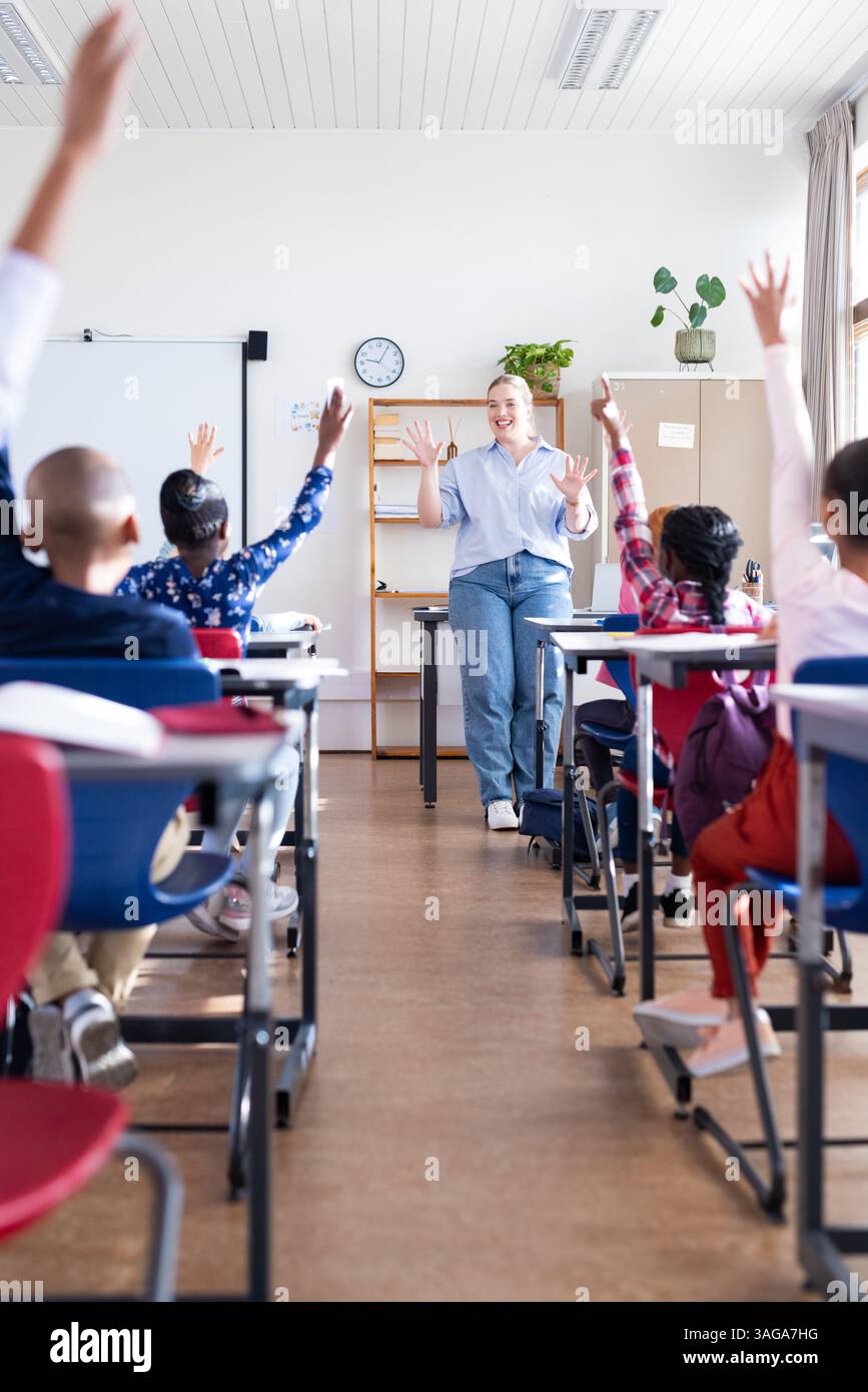 Coinvolgere studenti diversi in classe, insegnante donna alzando la mano e partecipando alla scuola Foto Stock