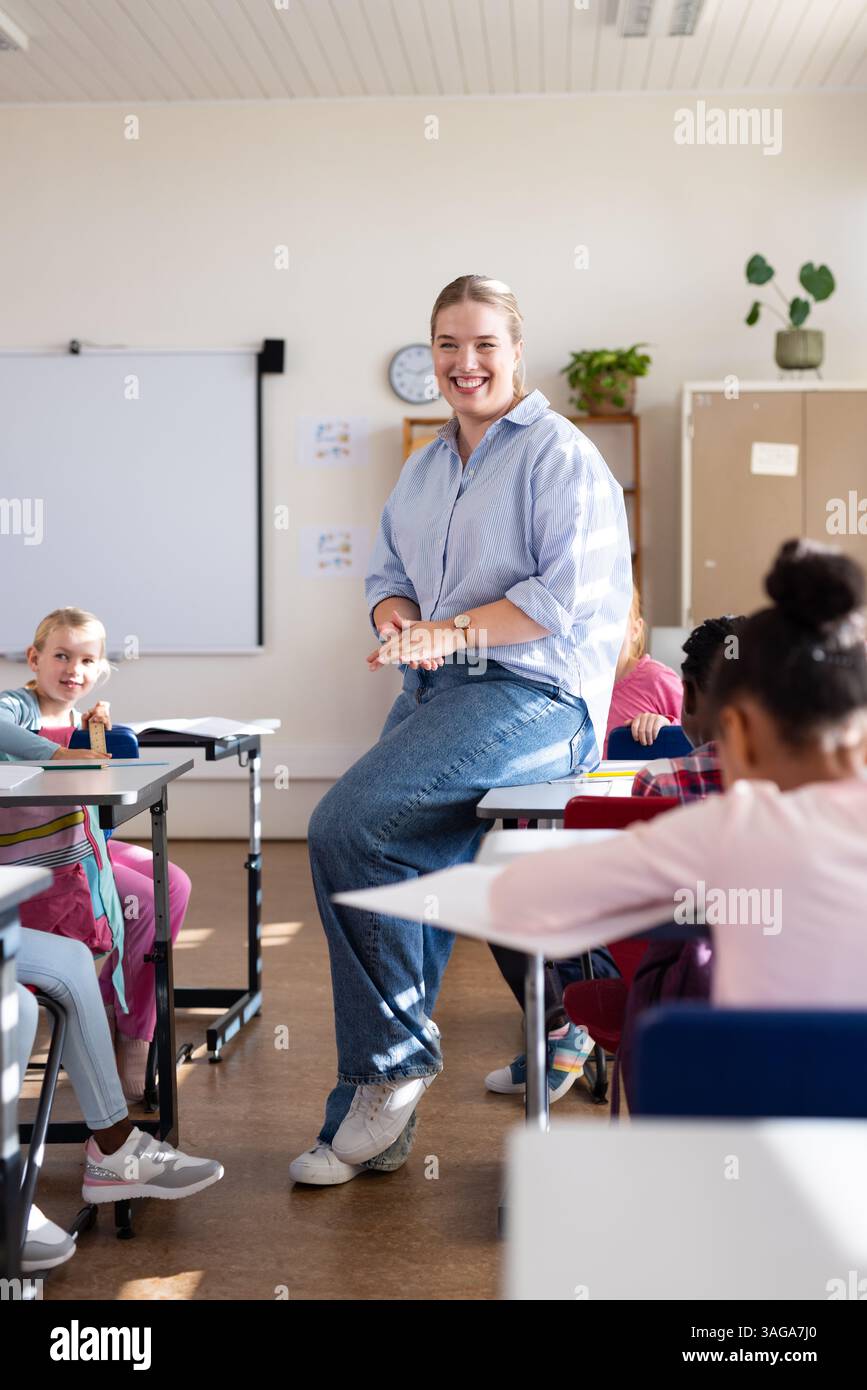 A scuola, un'insegnante sorridente e coinvolgente con studenti diversi in aula Foto Stock