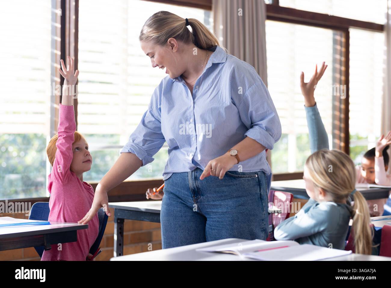 A scuola, alzando le mani, insegnante femminile che promuove la partecipazione attiva con studenti diversi Foto Stock