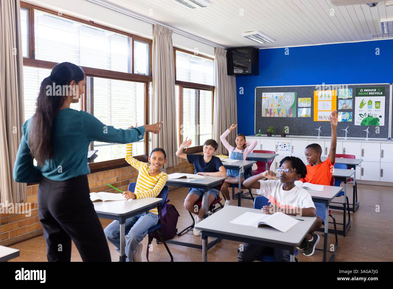A scuola, gli studenti alzano la mano per rispondere alla domanda dell'insegnante in classe Foto Stock