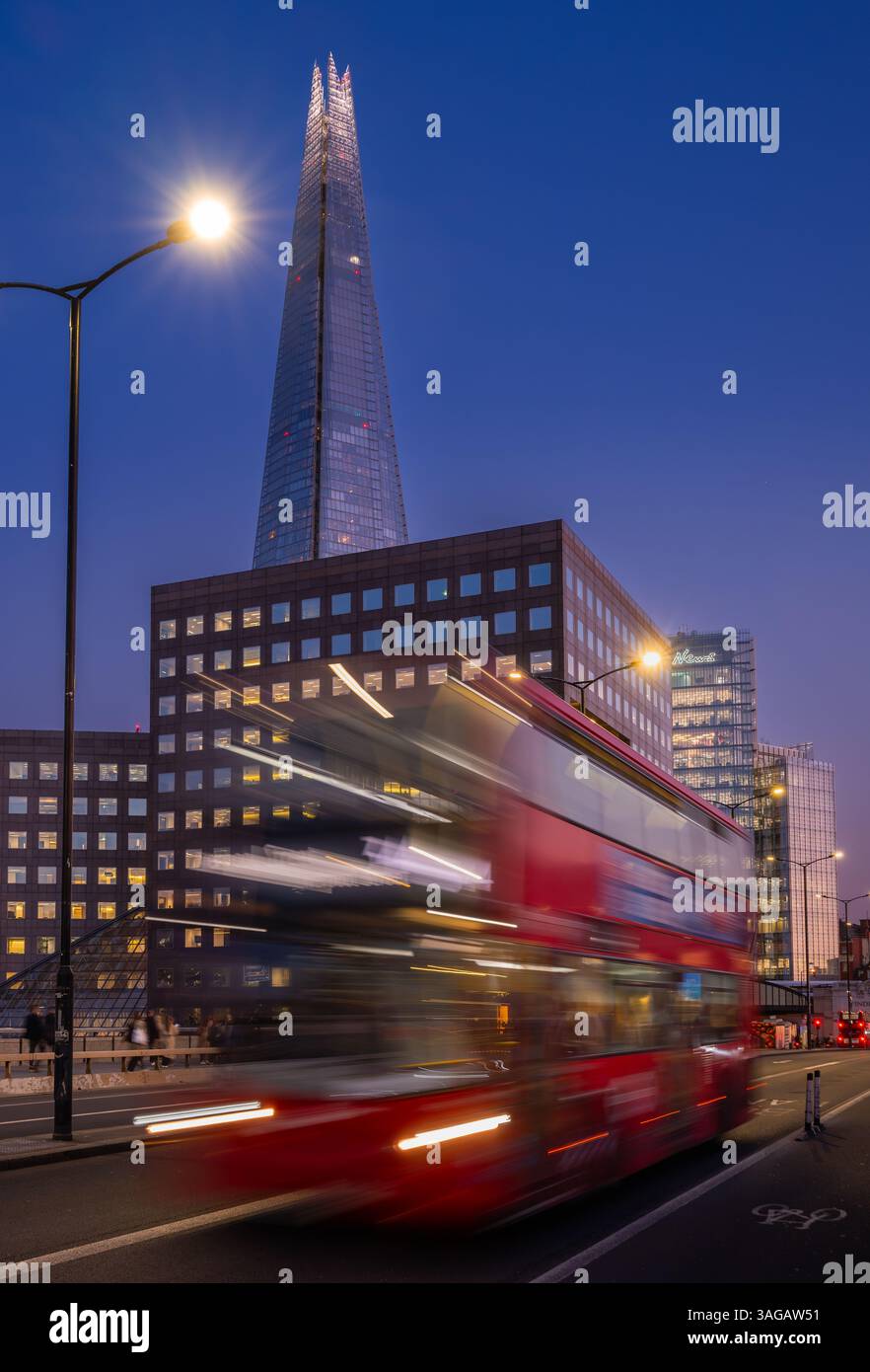 Londra, Regno Unito: Autobus rosso sul London Bridge con movimento sfocato al tramonto. Lo Shard e il London Bridge n. 1 dietro. Foto Stock