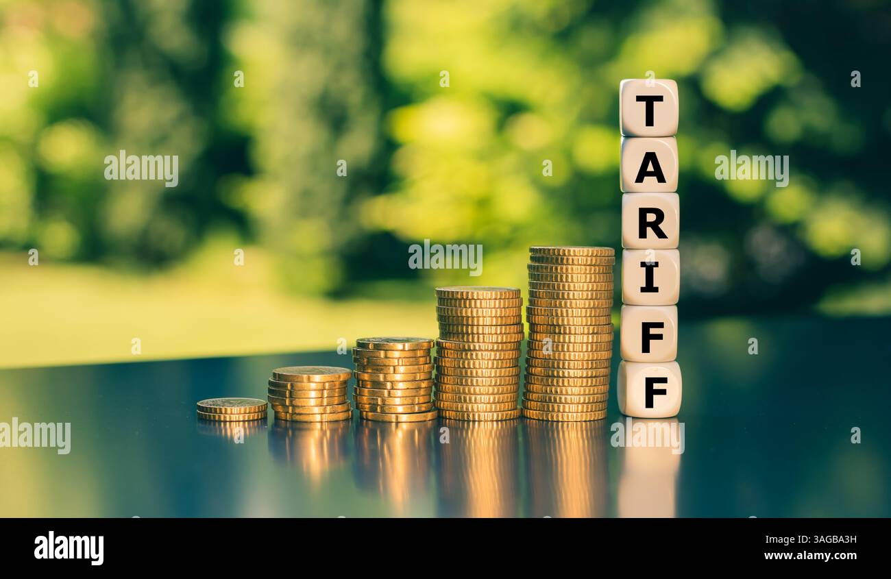 I dadi formano la parola Tariff accanto all'aumento di alte pile di monete. Simbolo delle crescenti tariffe statunitensi sulle merci internazionali. Foto Stock