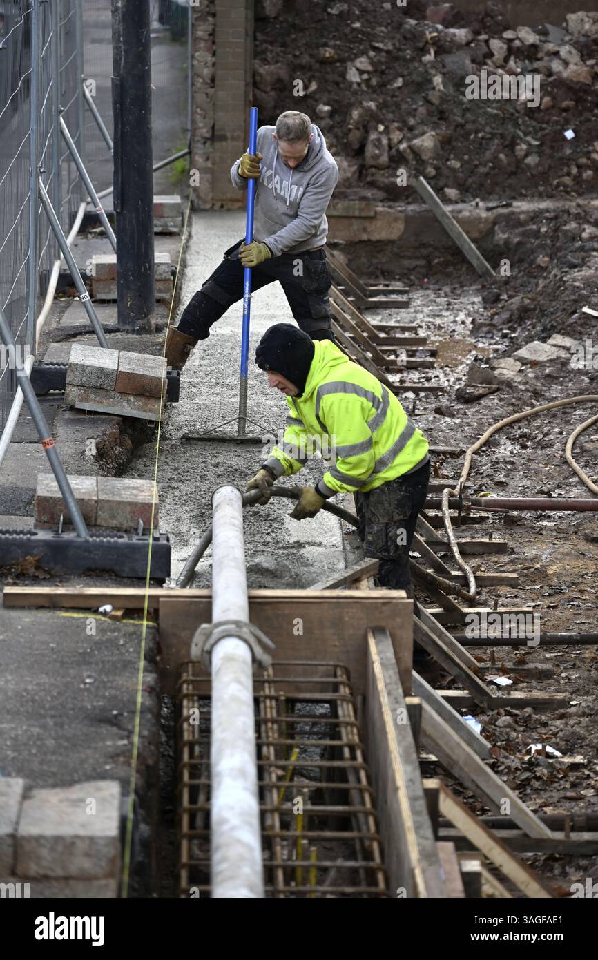 I costruttori livellano il calcestruzzo pompato che entra nella trave rinforzata in acciaio con copertura in legno e compattano con una macchina vibrante in cantiere Foto Stock
