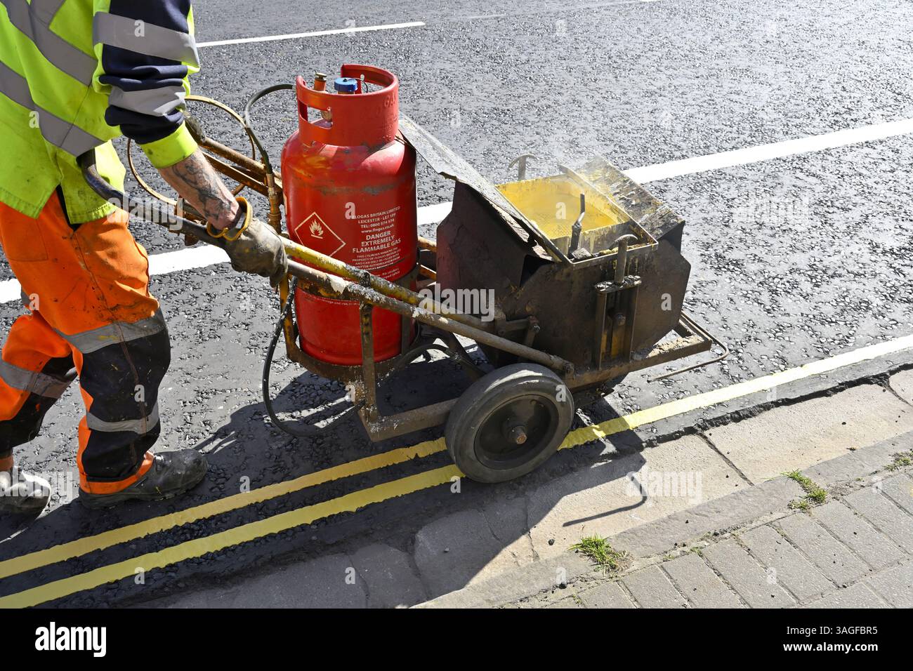 Verniciatura a linee gialle sul lato della strada (nessuna fermata, doppie linee gialle) con vernice fusa calda Foto Stock