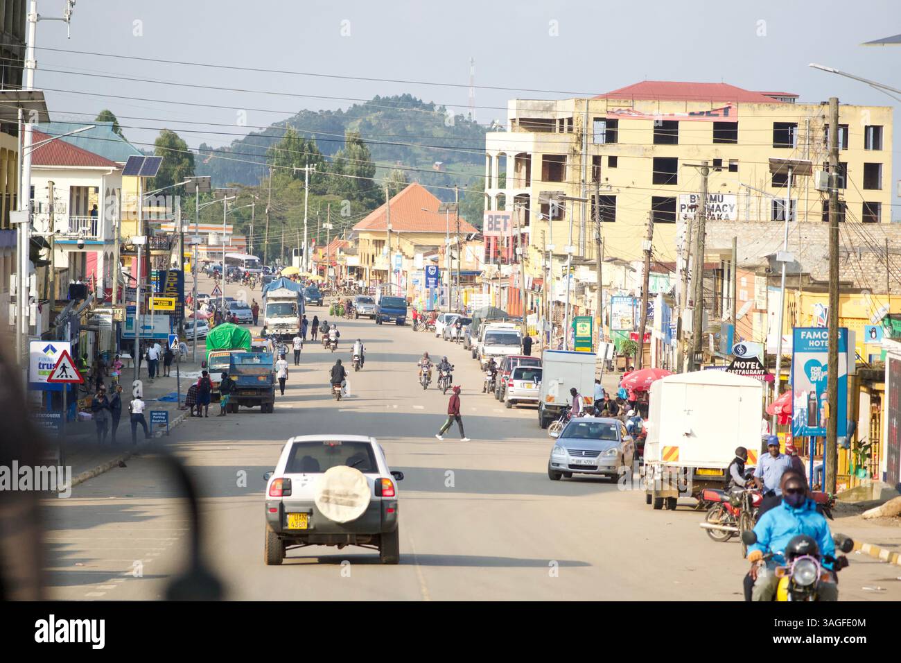 strada in Africa piena di auto e moto in una piccola città con case di medie dimensioni Foto Stock