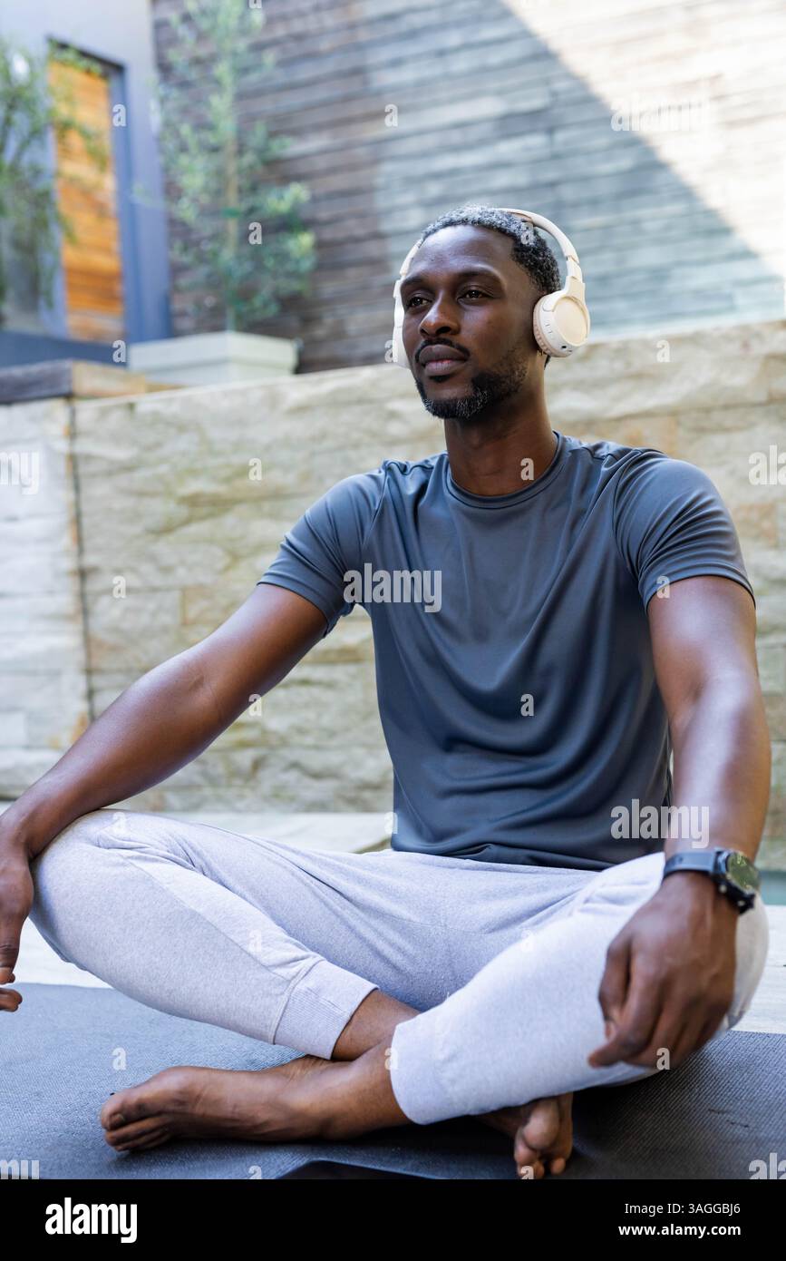 Meditando con le cuffie, un afroamericano afroamericano che si rilassa a bordo piscina nella pace mattutina. Consapevolezza, relax, tranquillità, benessere, c Foto Stock