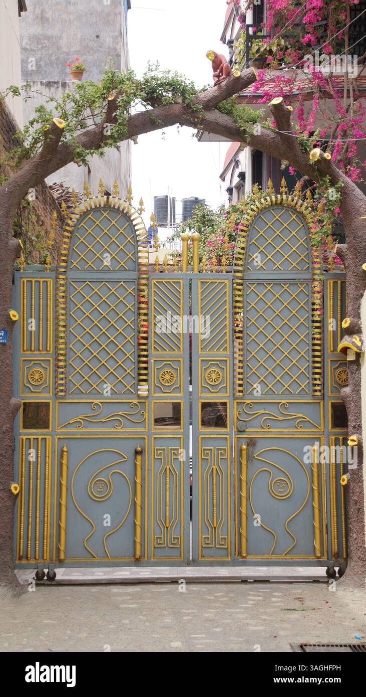 Cancello decorativo in metallo con motivi dorati ornati e un arco fiorito in una strada residenziale urbana Foto Stock