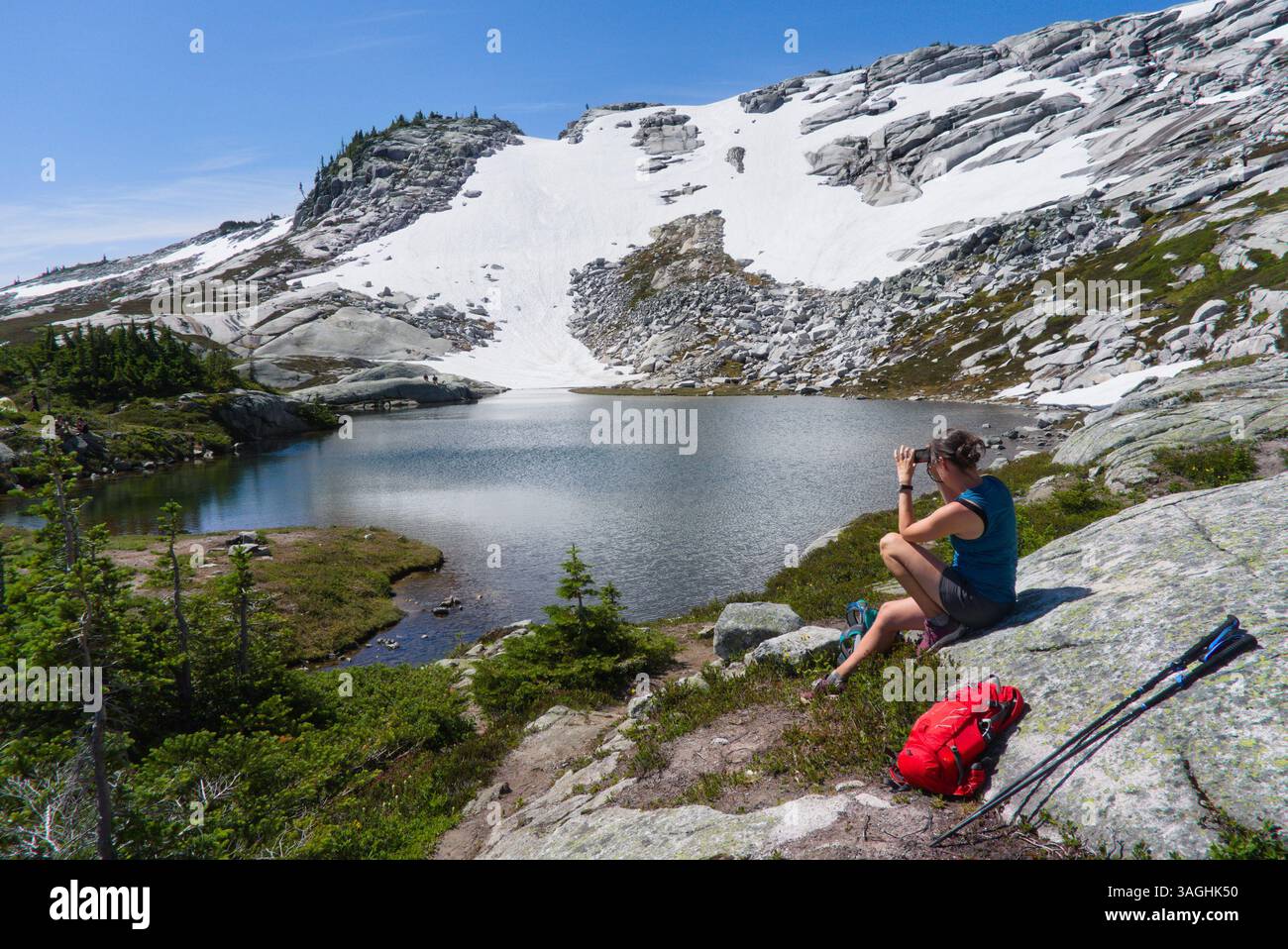 Escursionista donna che scatta foto del lago alpino vicino a Flatiron Peak, Coquihalla Summit Recreation area, British Columbia, Canada Foto Stock