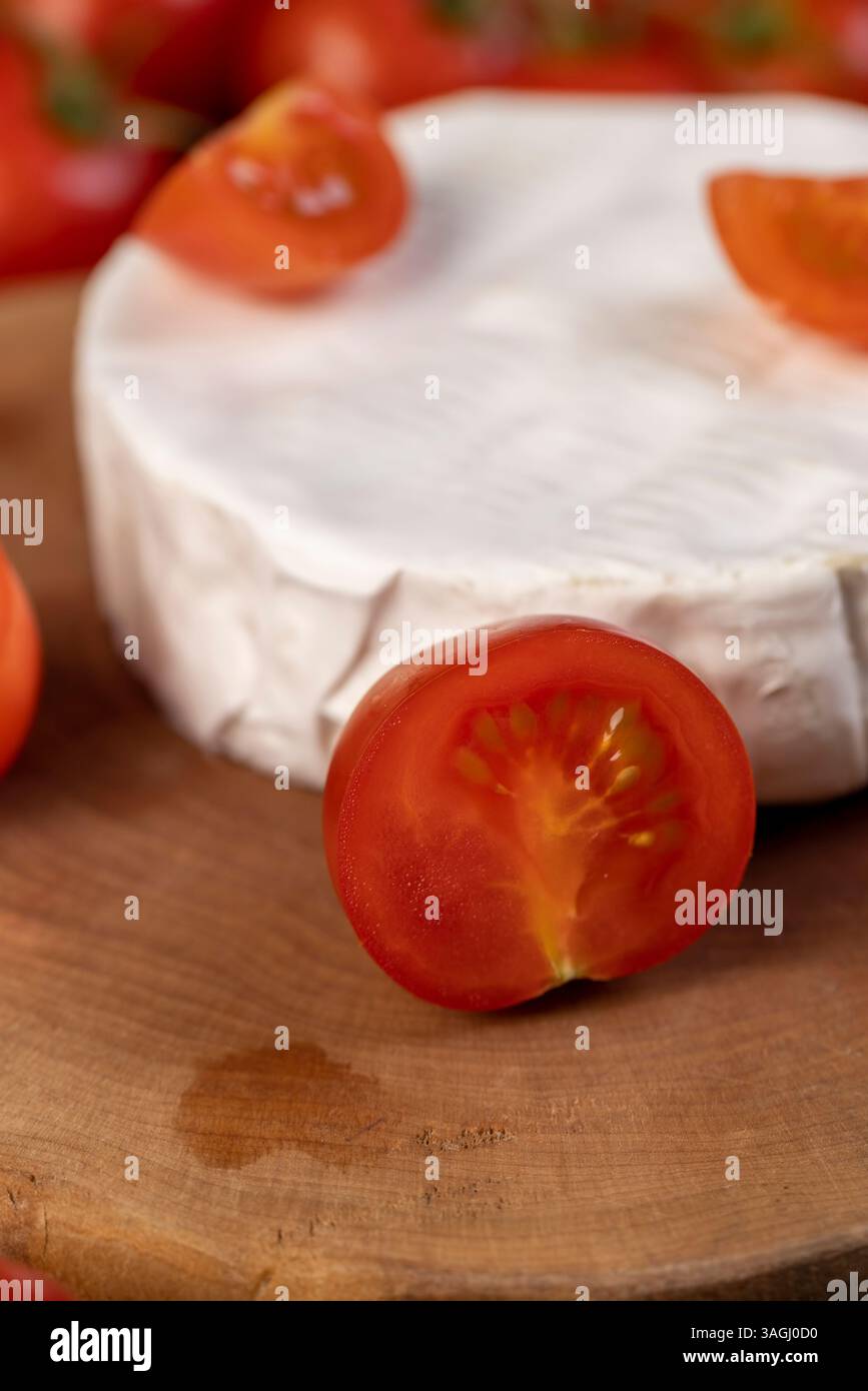 Formaggio con muffa e piccoli pomodori rossi, un pezzo di formaggio morbido maturo e alcuni piccoli pomodori rotondi rossi sul tavolo, concentrati sulla vista laterale del pomodoro Foto Stock