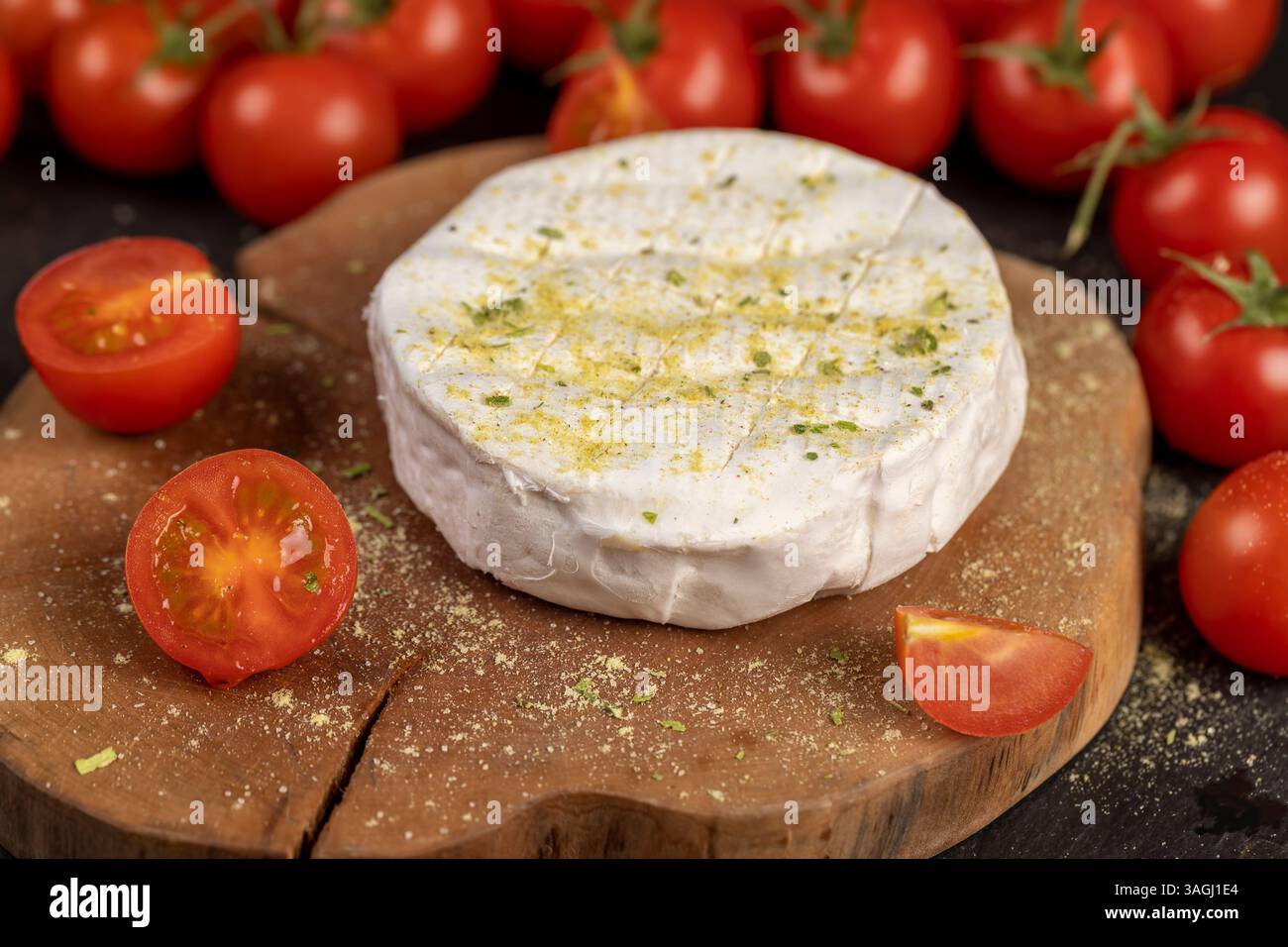formaggio morbido con muffa cosparsa di spezie e piccoli pomodori rossi maturi, formaggio morbido bianco con sale e spezie e pomodori rotondi rossi piccoli sul tabl Foto Stock