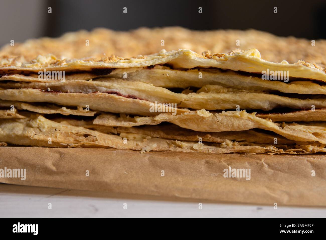 Processo di supporto. Primo piano degli strati di pasta sfoglia della deliziosa torta francese Napoleone stesa sulla carta di supporto. Pasticceria francese con burro crema pasticcera Foto Stock