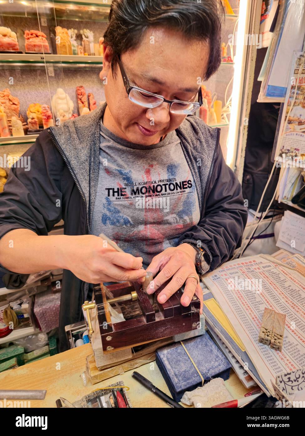 Un artigiano che lavora su sigilli cinesi tradizionali in pietra esposto in un negozio di artigianato a Man Wa Lane nel quartiere centrale di Hong Kong. Foto Stock