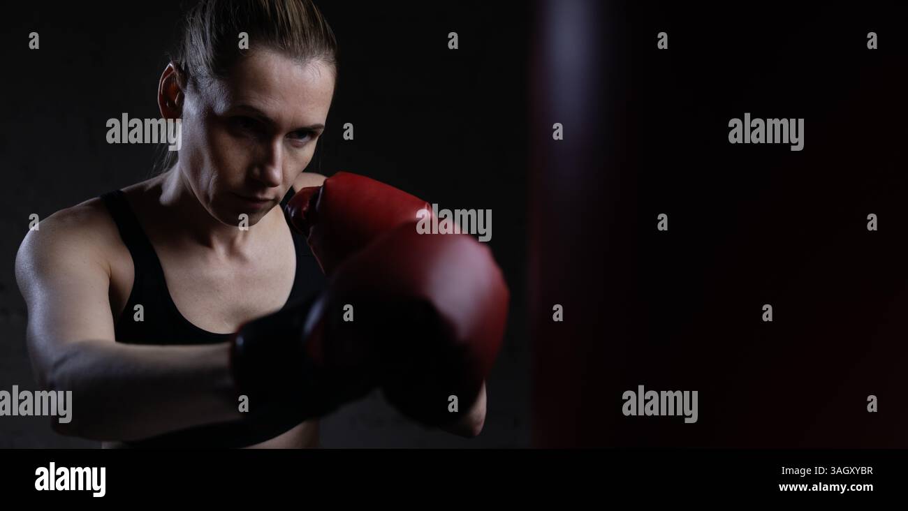 donna determinata a pugilare con guanti e borsone in palestra. formazione su potenza, resistenza e coordinamento. copia spazio Foto Stock