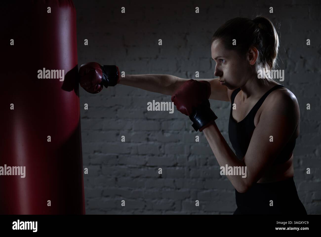 donna determinata a pugilare con guanti e borsone in palestra. formazione su potenza, resistenza e coordinamento Foto Stock
