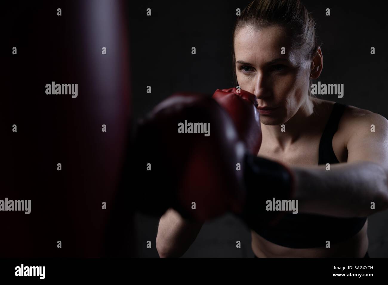 donna determinata a pugilare con guanti e borsone in palestra. formazione su potenza, resistenza e coordinamento Foto Stock