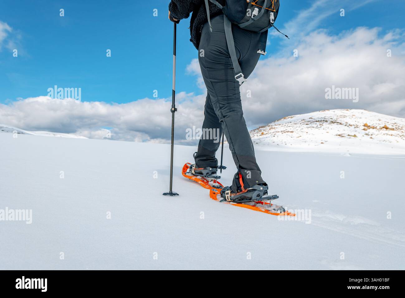 Vista posteriore ad angolo basso di una persona che cammina con le racchette da neve in una pianura innevata nella Sierra de Gredos, Spagna. Indossa pantaloni neri e racchette da neve arancioni Foto Stock
