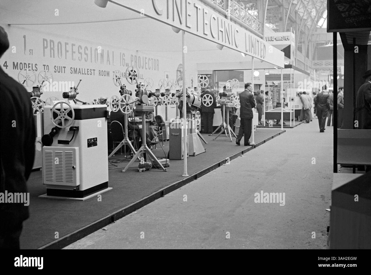 Visitatori a una fiera per produttori e fornitori di film e fotografie a Olympia, West Kensington, Hammersmith, Londra, Inghilterra, Regno Unito in c.1960. Presso lo stand Cinetechnic erano esposti proiettori cine professionali da 16 mm. Dietro c'è uno stand per View-Master, un'azienda specializzata in visori stereoscopici per immagini fisse a colori di piccole dimensioni (su bobine di dischi di cartone), ancora oggi popolare (ora prodotta da Mattel). Questo proviene dal vecchio negativo in bianco e nero di un fotografo amatoriale - una fotografia vintage anni '1950/'60. Foto Stock