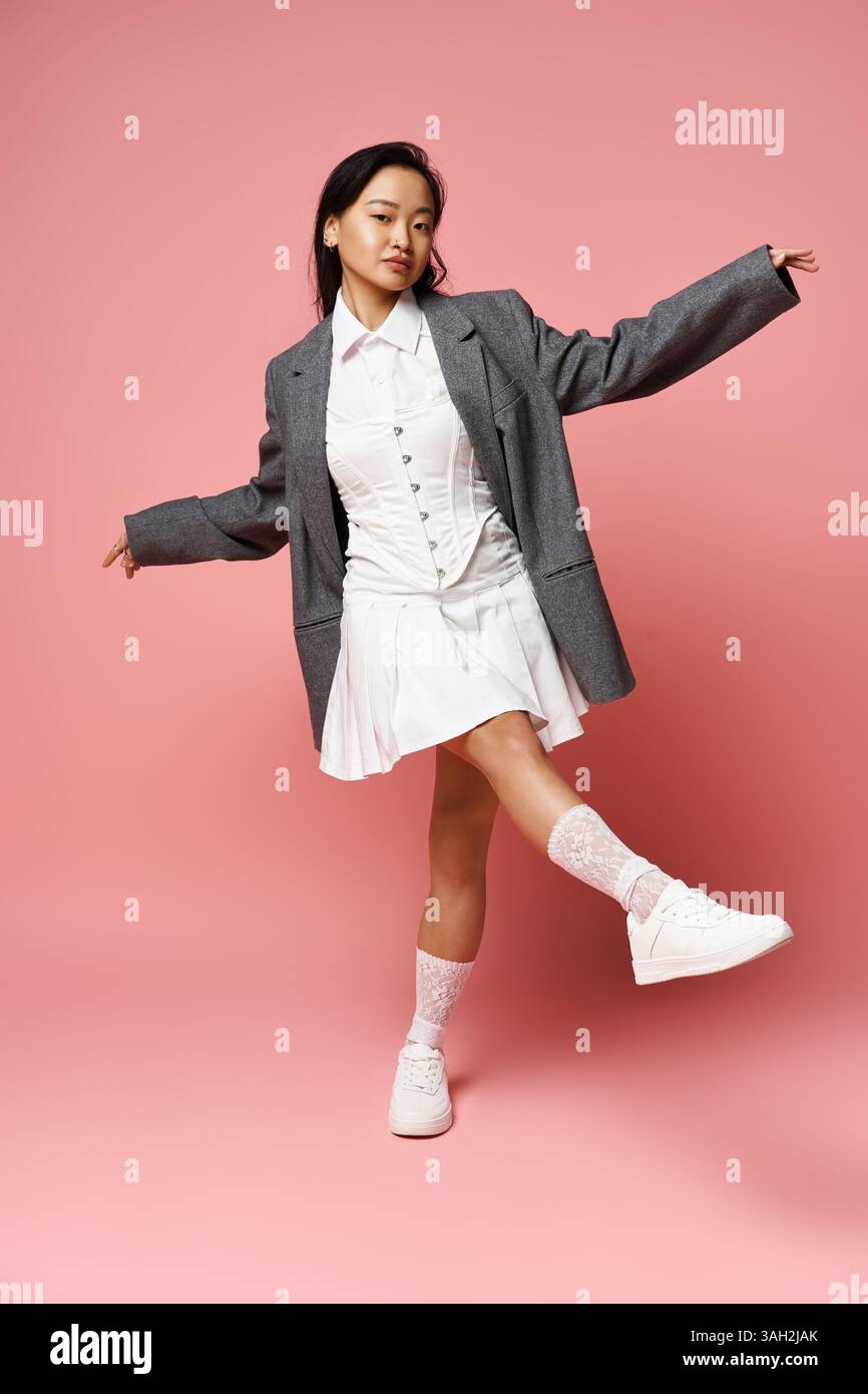 Una bella giovane donna asiatica posa giocosamente, vestita con un outfit alla moda con un blazer grigio. Foto Stock