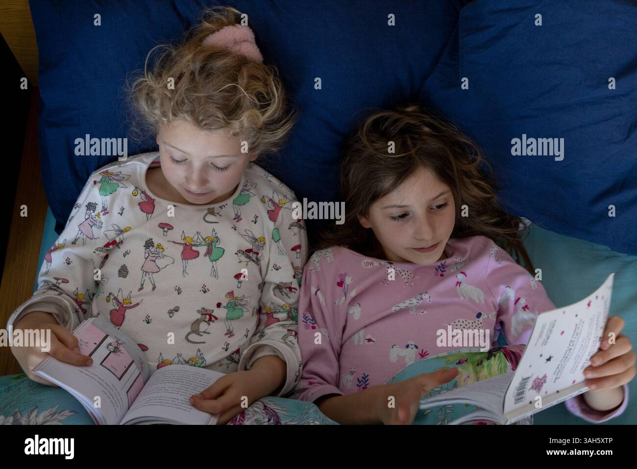 Due sorelle di bambini che leggono libri a letto fianco a fianco. Le ragazze hanno 7 anni (a sinistra) e 9. Foto Stock