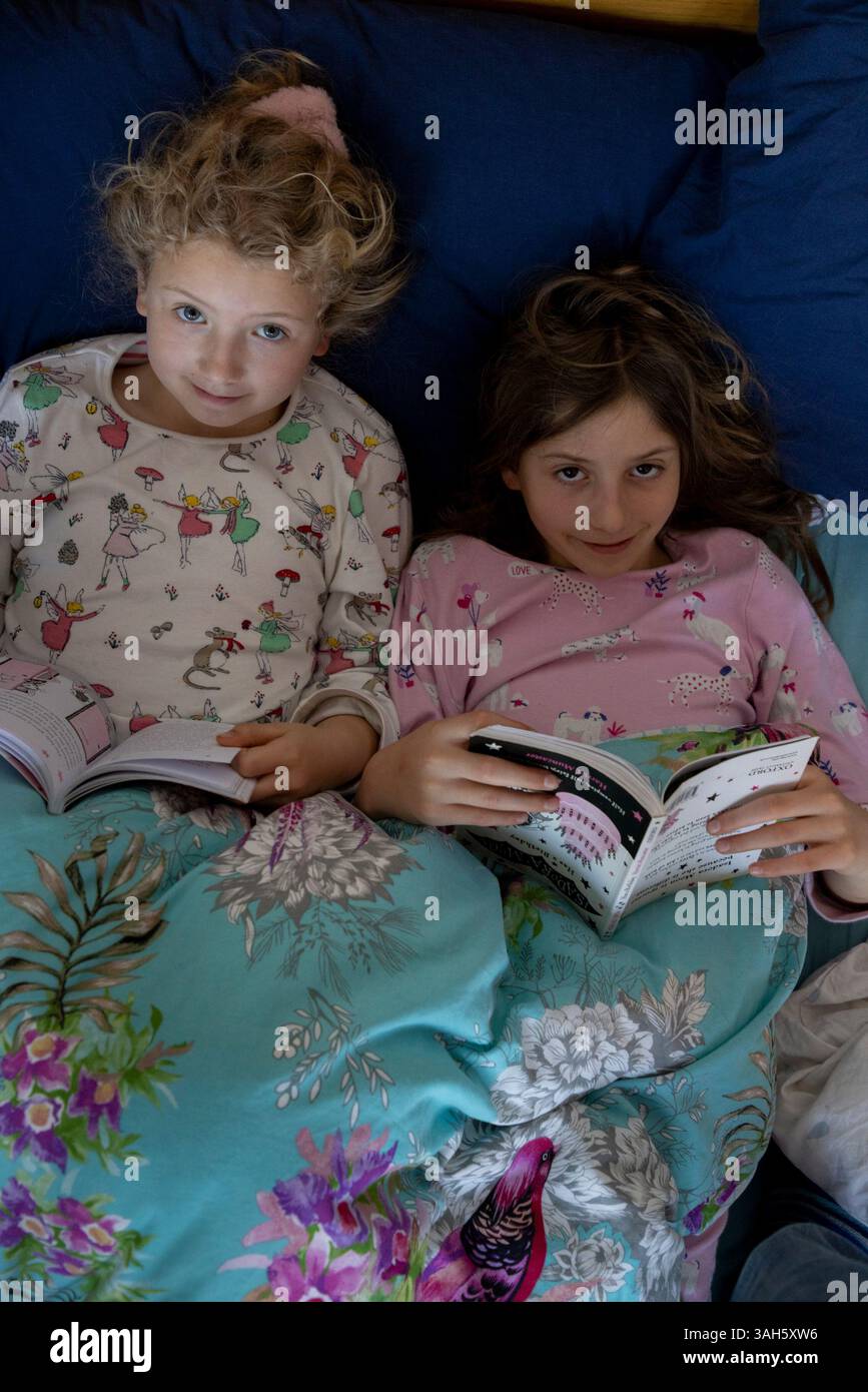 Due sorelle di bambini che leggono libri a letto fianco a fianco. Le ragazze hanno 7 anni (a sinistra) e 9. Foto Stock
