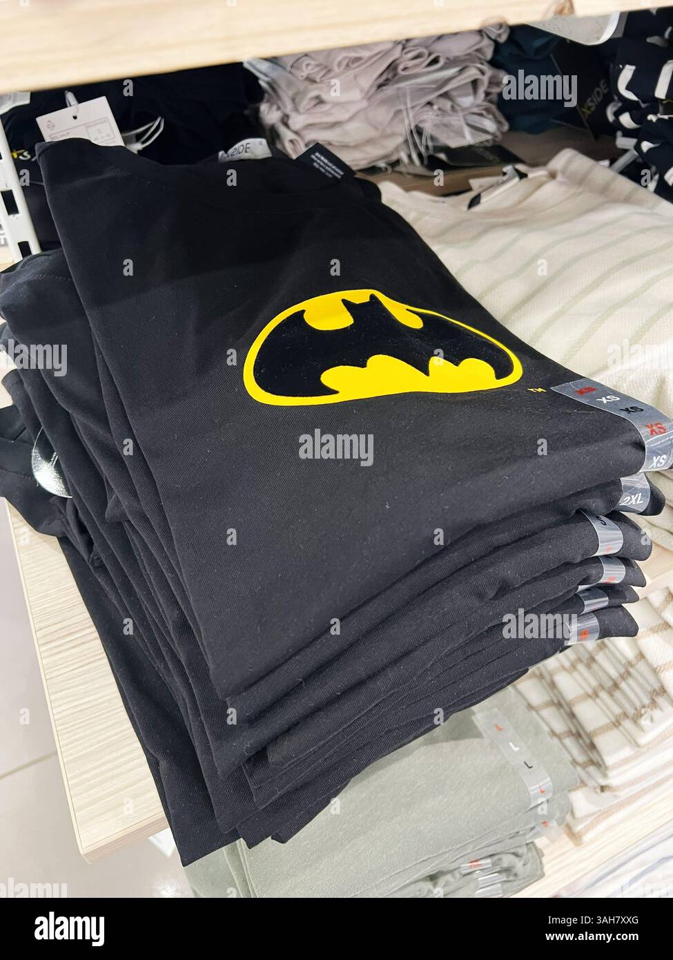 Kiev, Ucraina - 8 aprile 2025: Pile di t-shirt nere con l'iconico logo Batman disposte ordinatamente su scaffali in legno. Foto Stock