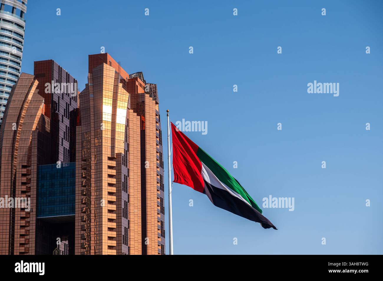 Bandiera degli Emirati Arabi Uniti che sventola sul cielo blu, alti edifici sullo sfondo di Abu Dhabi Foto Stock