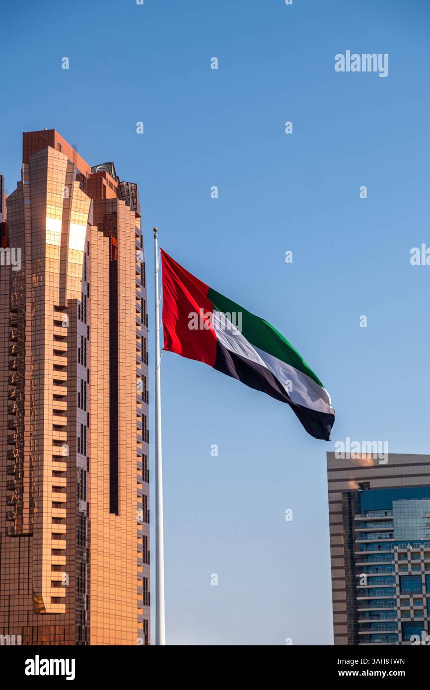 Bandiera degli Emirati Arabi Uniti che sventola sul cielo blu, alti edifici sullo sfondo di Abu Dhabi Foto Stock