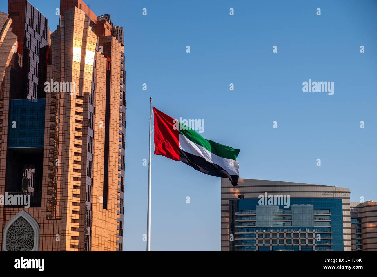 Bandiera degli Emirati Arabi Uniti che sventola sul cielo blu, alti edifici sullo sfondo di Abu Dhabi Foto Stock