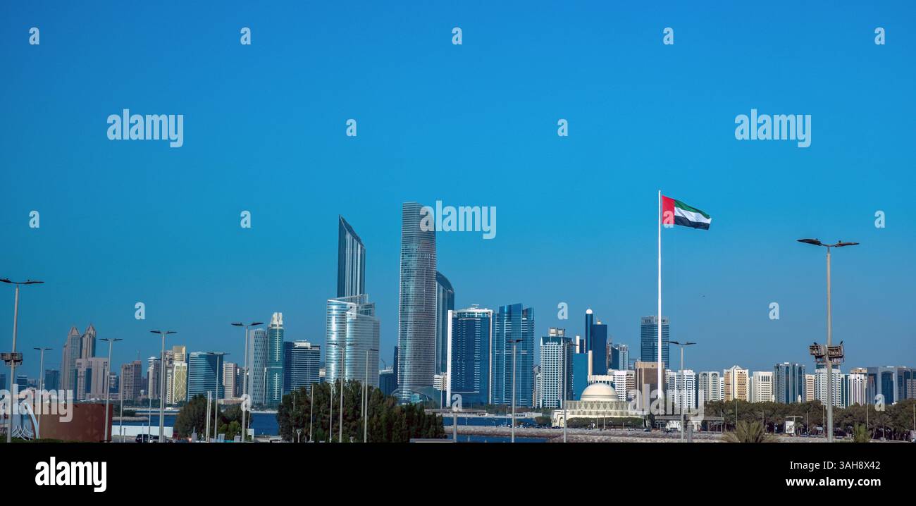 Abu Dhabi. Bandiera degli Emirati Arabi Uniti, alti edifici moderni, palme e cielo blu. Emirati Arabi Uniti. Foto Stock