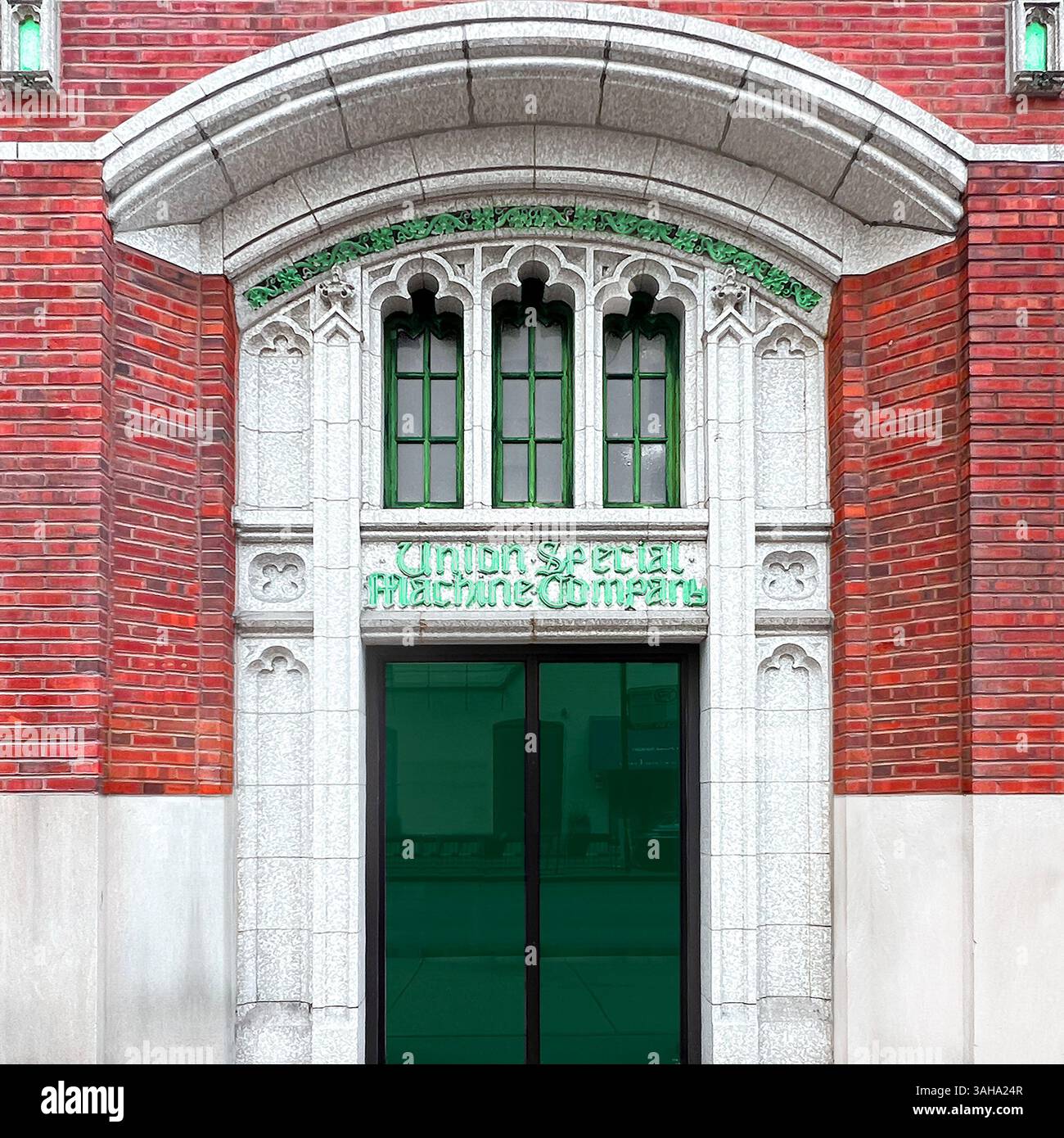 Ingresso verde in stile neogotico con trafori in pietra ad arco, finestre verticali e cartellone storico "Union Special Machine Company" incorporato in mattoni. Foto Stock