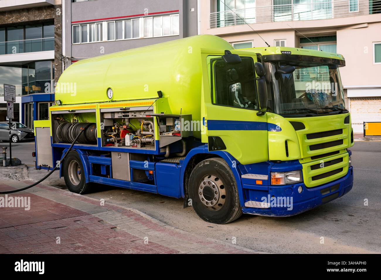 Camion luminoso con un grande serbatoio del gas e un vano attrezzatura aperto parcheggiato su una strada cittadina, che eroga gas attraverso un tubo flessibile collegato. Foto Stock