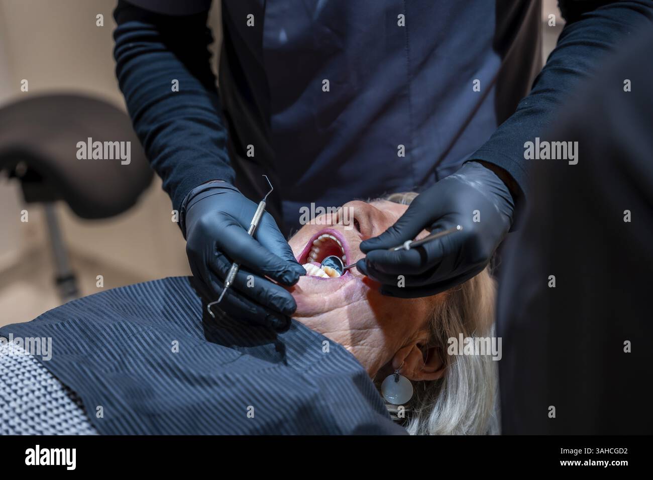 Dentista che indossa guanti neri che esaminano i denti di una donna anziana sdraiata su una sedia dentista durante un check-up Foto Stock