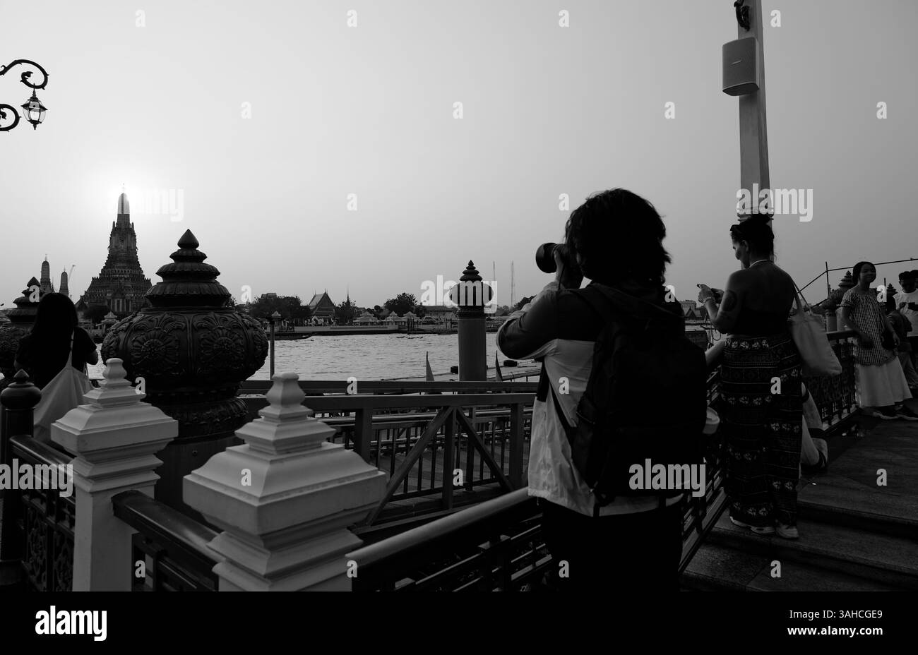 I turisti fiancheggiano il fiume per fotografare il tramonto dietro Wat Arun Foto Stock