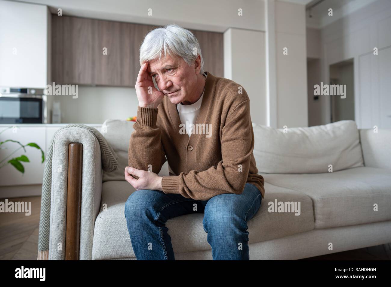Pensionato anziano depresso tiene la testa in mano seduto da solo sul divano di casa. Abbandono sociale Foto Stock