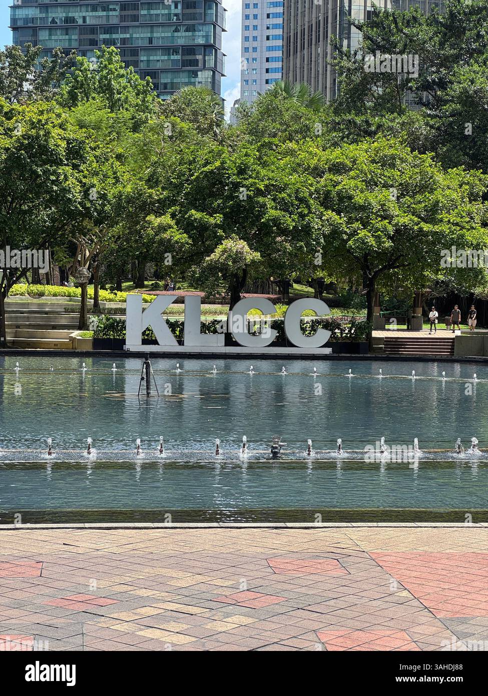 Cartello KLCC riflesso nello stagno con fontana a Kuala Lumpur. Un punto di riferimento moderno nel cuore della capitale della Malesia. - Immagine stock catturata con smartphone