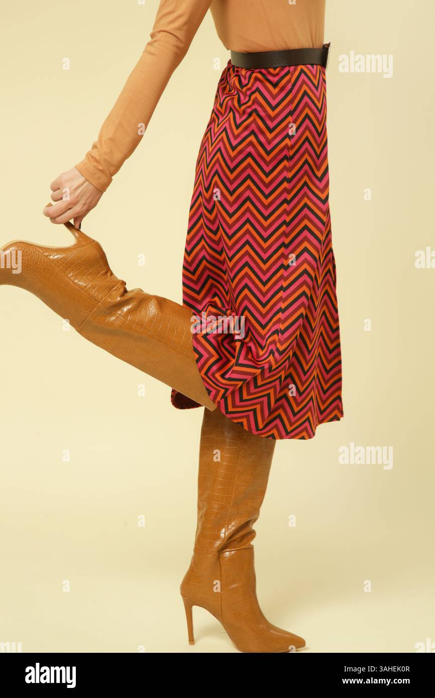 Serie di foto in studio di una modella femminile che indossa una camicia dolcevita beige e una gonna longuette a motivi rossi con fessura, stile retrò anni '70 Foto Stock