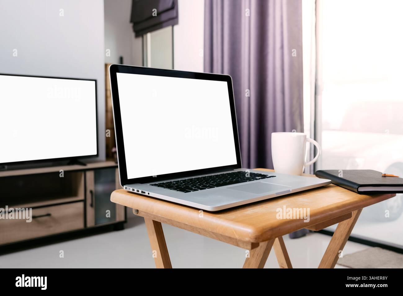 lavorate a casa usando un computer portatile su una piccola scrivania di fronte alla televisione nel soggiorno della mia casa con un caffè serale. Foto Stock
