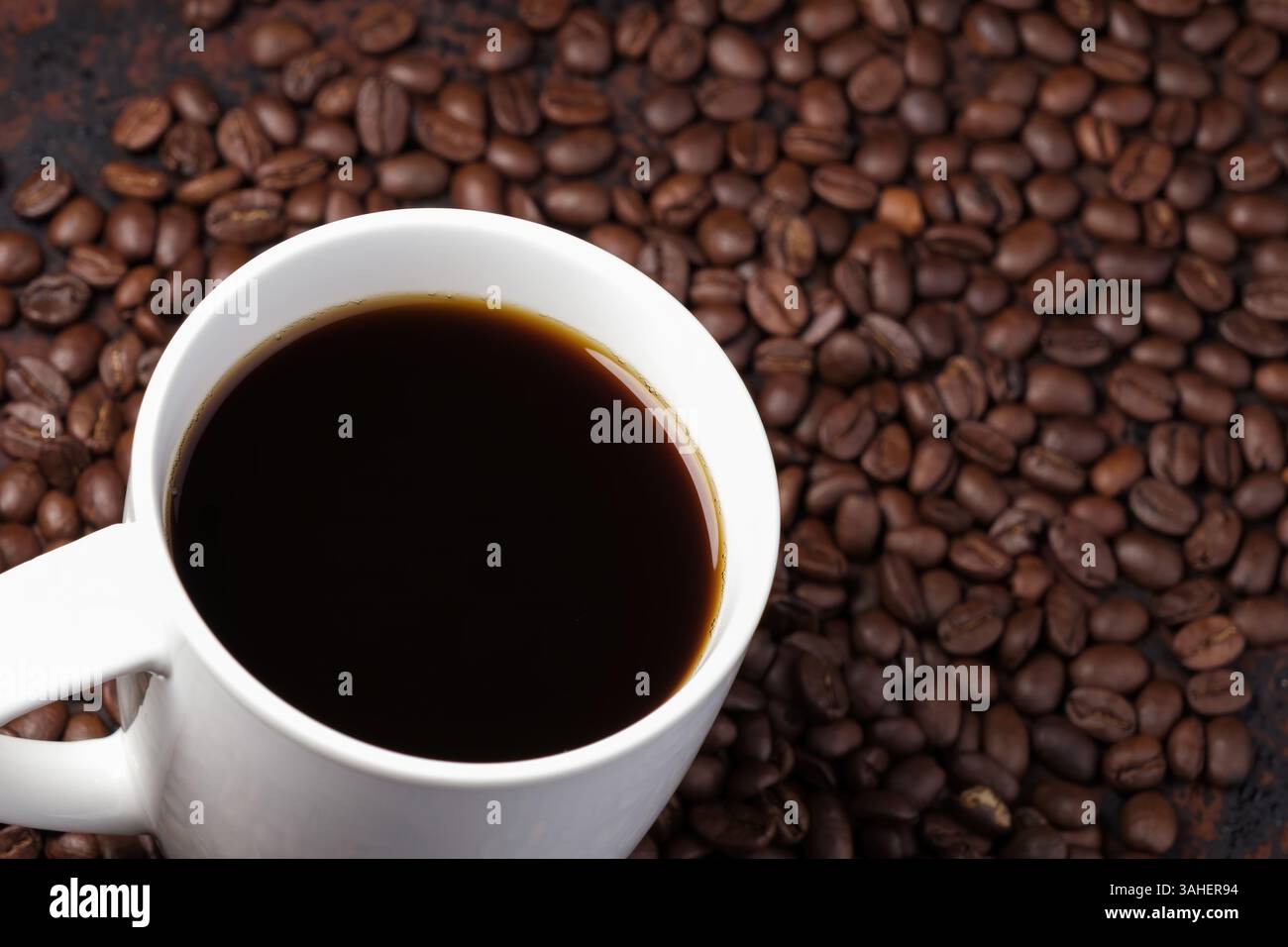 caffè nero in tazza bianca circondato da chicchi di caffè tostati su un tavolo di legno rosso scuro Foto Stock