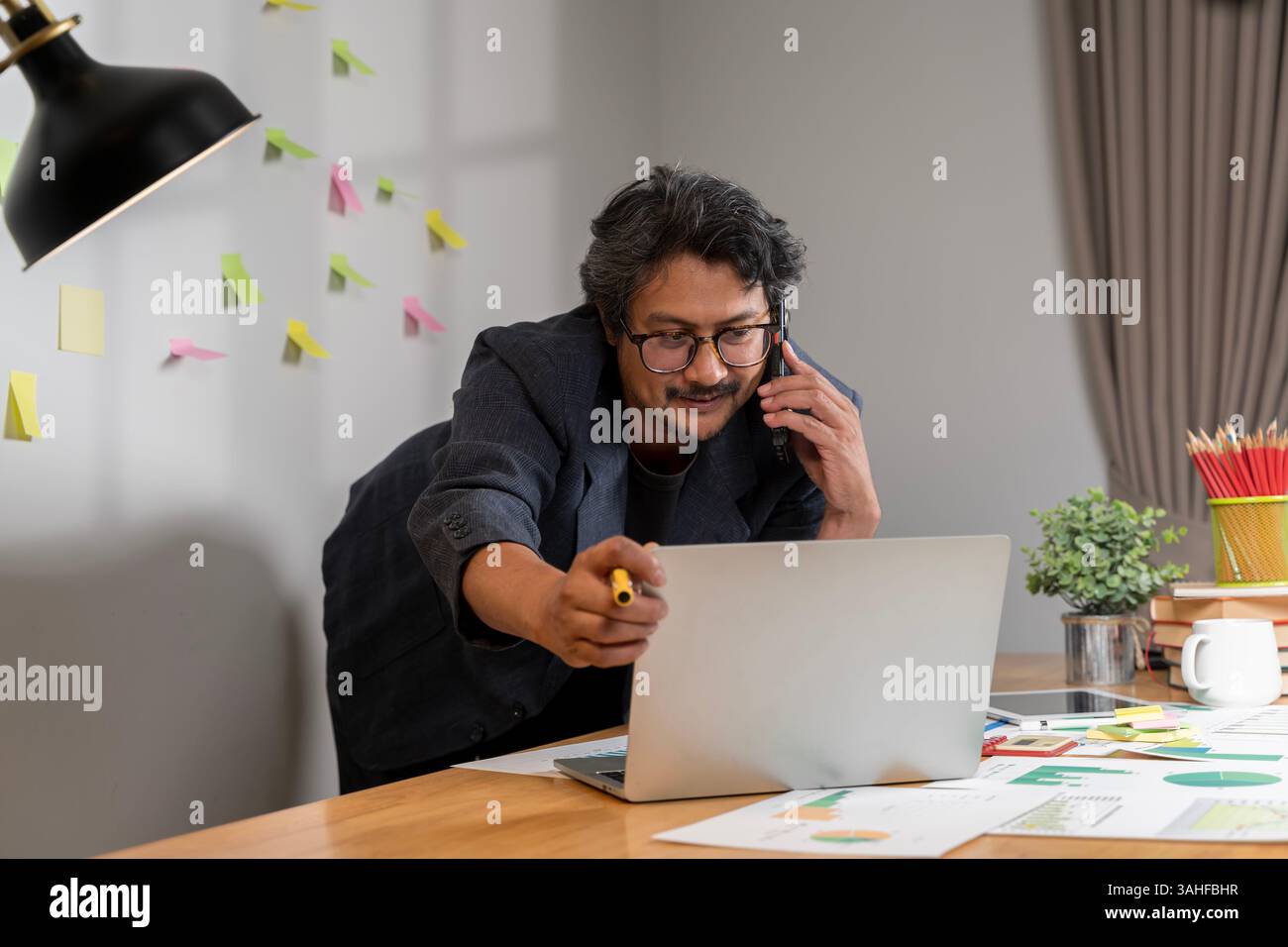 Giovane e allegro professionista che lavora intensamente in un ambiente d'ufficio moderno. Un uomo caucasico medio adulto in abbigliamento da lavoro lavora intensamente su un l Foto Stock