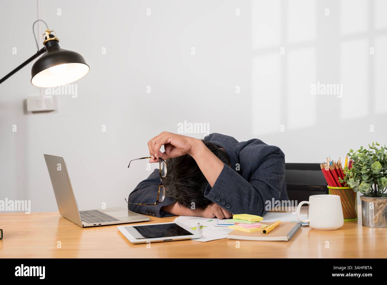 Uomo d'affari affaticato con disturbi del sonno che dorme alla scrivania. Uomo d'affari che dorme sul computer portatile alla scrivania in ufficio. Privazione del sonno e straordinari ov Foto Stock