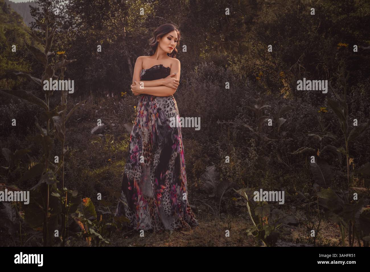 Bella giovane donna asiatica che trasuda eleganza mentre si mette in posa nel tranquillo ambiente della foresta, avvolto in una tavolozza di colori tenui e caldi Foto Stock
