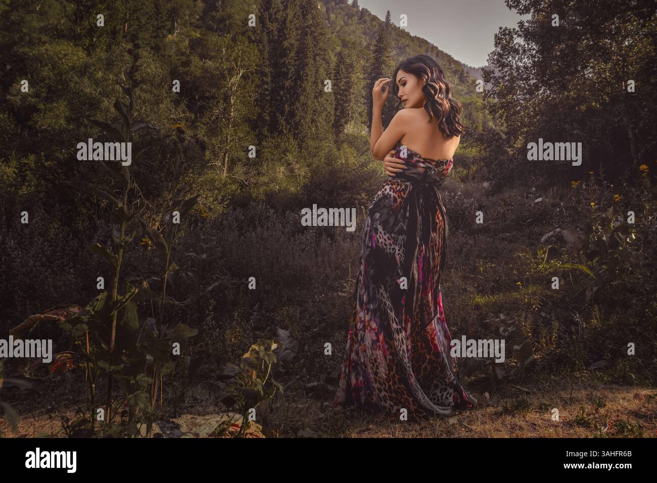 Bella giovane donna asiatica che trasuda eleganza mentre si mette in posa nel tranquillo ambiente della foresta, avvolto in una tavolozza di colori tenui e caldi Foto Stock
